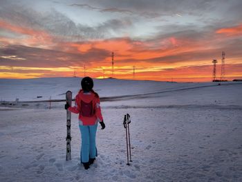 Woman skier holding her skis while watching the sunset