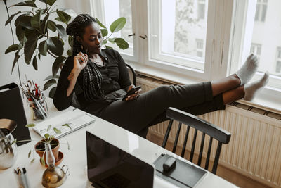 Young businesswoman text messaging through smart phone while sitting in home office