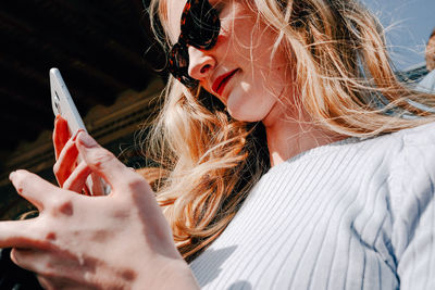 Low angle view of woman in sunglasses using smart phone on sunny day