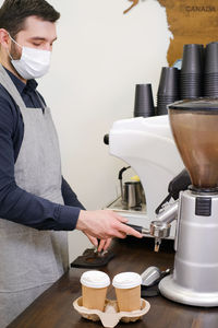 Barista serving coffee in takeaway cups in coffee shop in protective mask. coffee to go during