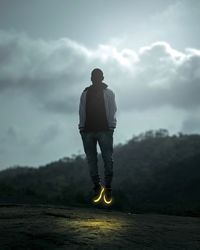 Rear view of man standing on mountain against sky