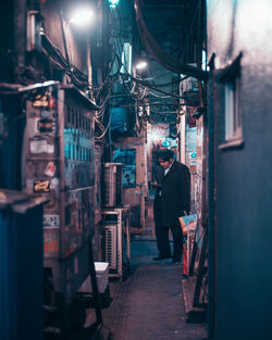 Rear view of man standing on illuminated street amidst buildings at night