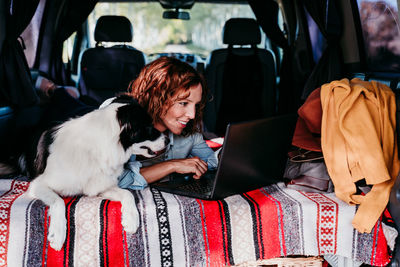 Woman using laptop while lying with dog in camper trailer