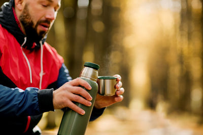 Close-ups of a man pouring tea into a cup from a thermos while relaxing in an autumn park or forest