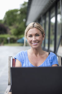 Portrait of happy woman sitting with laptop at yard