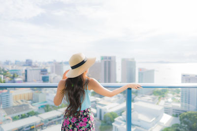 Rear view of woman looking at cityscape against sky