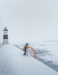 Woman standing on jetty by lighthouse against sky during winter