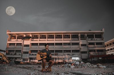 Woman sitting against building against sky