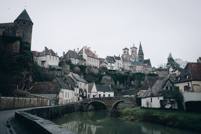 Bridge over river amidst buildings in town against clear sky