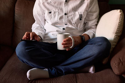 Close-up of a young man looking at his smartphone sitting on a couch