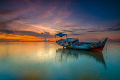 Boat moored in sea against sky during sunset