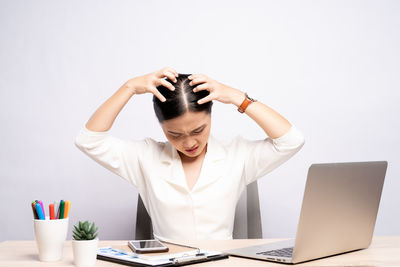 Young woman using phone while sitting on table against white background