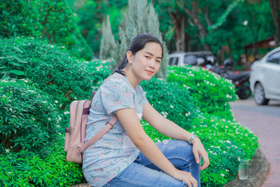 Portrait of smiling woman sitting by plants at roadside