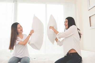 Happy friends pillow fighting on bed at home