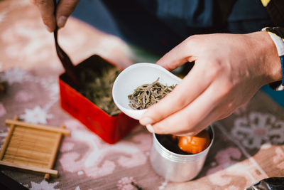 Close-up of hand holding bowl with tea leaves at table