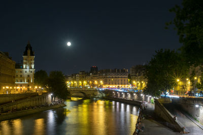 Illuminated bridge over river by buildings in city at night