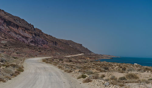 Scenic view of road by sea against clear blue sky