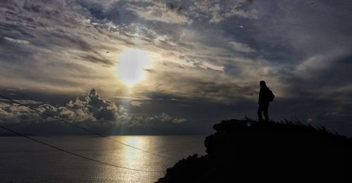 Silhouette man standing by sea against sky during sunset