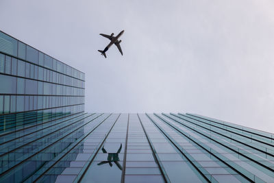 Low angle view of modern building against sky with airplane reflection 