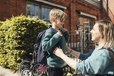 Happy mother looking at son with backpack outside school building