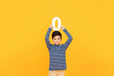 Portrait of boy standing against yellow background