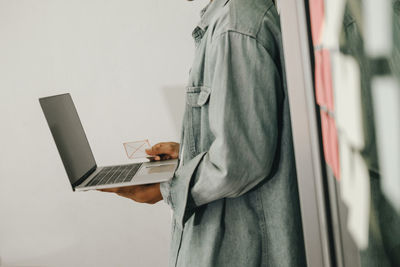 Side view of man using mobile phone against wall