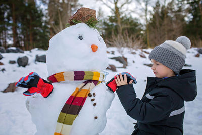 Boy in hat makes snowman, which was the nose of snowman, smiling. winter family weekend, lifestyle