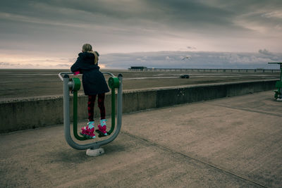 Rear view of girl standing on exercise equipment at promenade