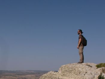 Full length of man standing on rock against clear blue sky