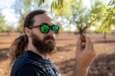 Young man looking at nutshell of almond while standing in agricultural field