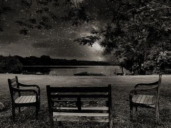 Empty bench in park by sea against sky