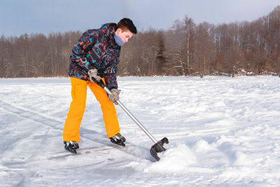 Full length of teenage boy ice-skating while cleaning snow