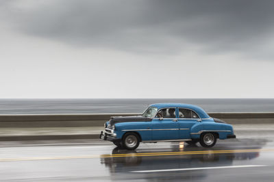 Car on road against sea and cloudy sky