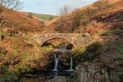 A waterfall and packhorse stone bridge at three shires head in the peak district national park.