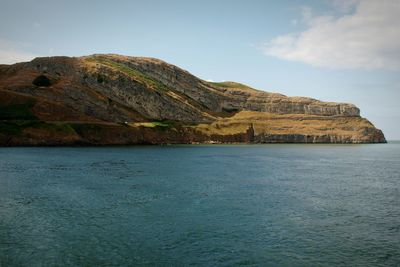 Scenic view of sea by mountain against sky