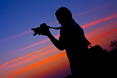 Silhouette man photographing against sky during sunset