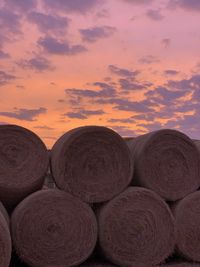 Stack of hay bales on field against sky during sunset