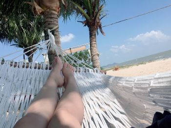 Low section of woman relaxing on hammock at beach against sky