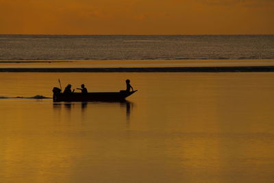 Silhouette men in sea against sky during sunset