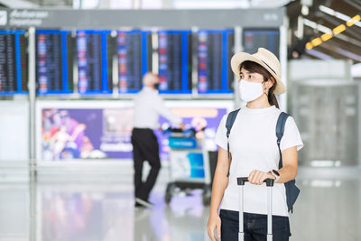 Woman wearing mask looking away while standing at airport