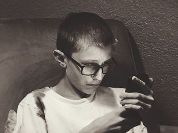 Close-up of boy using mobile phone against wall at home