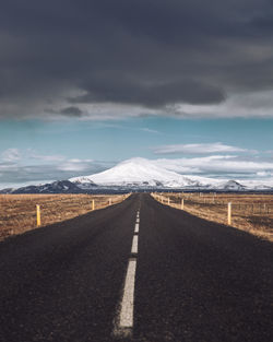 Empty road leading towards snowcapped mountains against sky