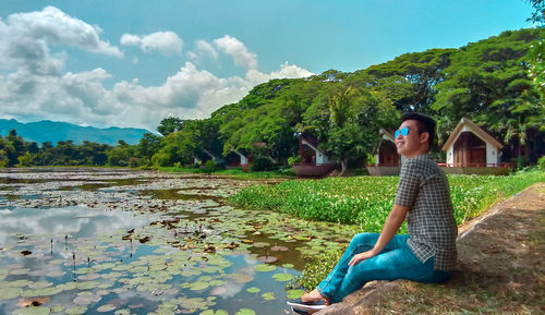 Side view of senior man sitting by lake against sky