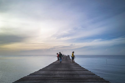 People on pier over sea against sky during sunset