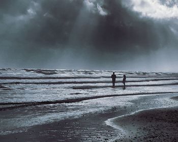 Silhouette people standing on beach against sky