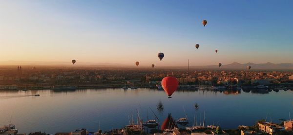 Hot air balloons flying over lake against sky during sunset