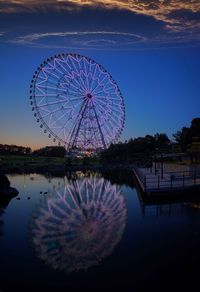 Ferris wheel by lake against clear blue sky at night