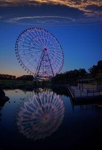 Ferris wheel by lake against clear blue sky at night