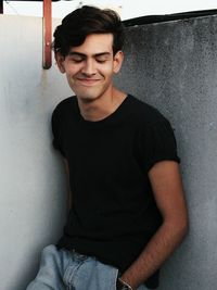 Portrait of smiling young man leaning against wall