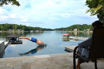 Man sitting on seat by lake against sky